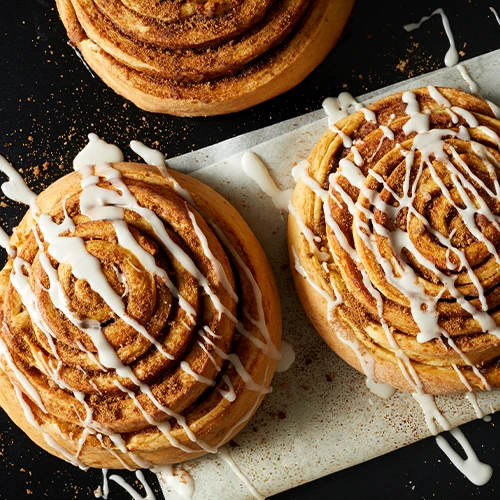 Three Cinnamon Rolls with icing drizzled on top ready to be eaten